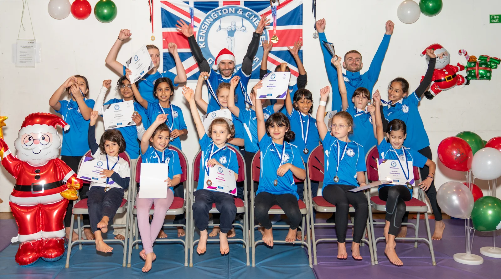 Coach Stefan and young gymnasts celebrating their achievements during the 2024 Christmas event at Kensington & Chelsea Gymnastics Club in London.