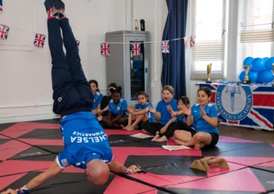 Coach Stefan Kolimechkov demonstrating a Japanese handstand in front of his gymnasts at KCGA London during the 2025 Annual Performance in Knightsbridge
