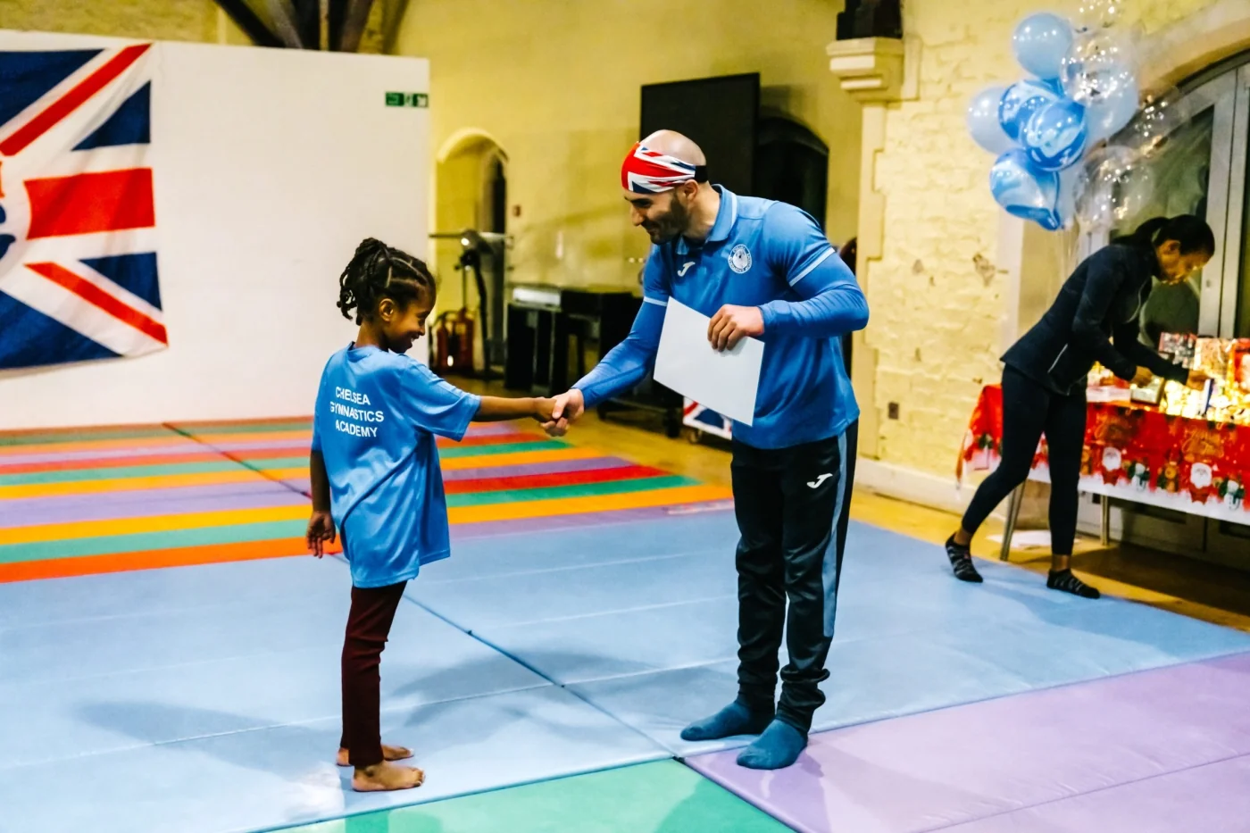 Coach and gymnast shake hands after performance during Chelsea Gymnastics Academy’s 2022 Christmas celebration.
