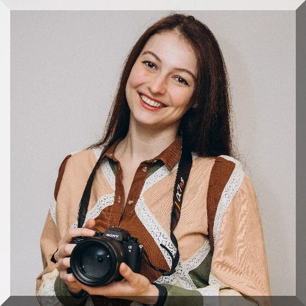 Kseniia, club photographer for Kensington & Chelsea Gymnastics, holding a camera and smiling.