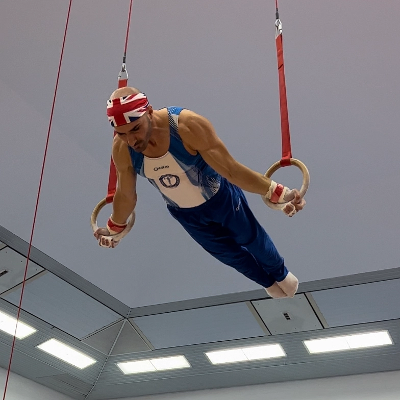 Stefan, director of Kensington and Chelsea Gymnastics Academy, performing a maltese cross on gymnastics rings during competition.