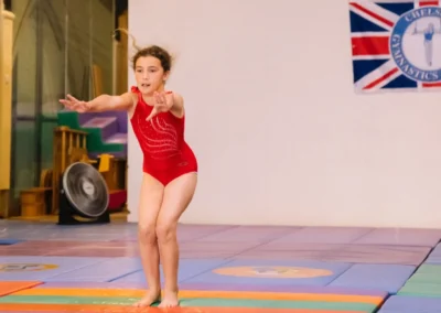 Young gymnast holding a landing position at the end of her floor routine during the Annual Performance 2023 at Kensington & Chelsea Gymnastics Academy.