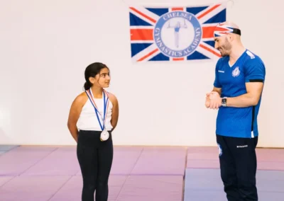 Coach Stefan presenting a special medal to a young gymnast, the longest-standing member of Chelsea Gymnastics Academy since 2022.