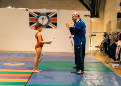 Young gymnast receiving certificate from coach during KCGA Easter awards ceremony in Kensington London W8.
