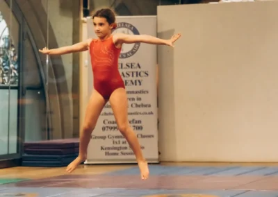 Young gymnast in red leotard performing star jump at KCGA Easter gymnastics event Kensington London W8.