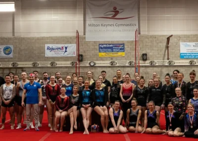 Large group of masters gymnasts and coaches posing on the competition floor at Milton Keynes Gymnastics, 2023.
