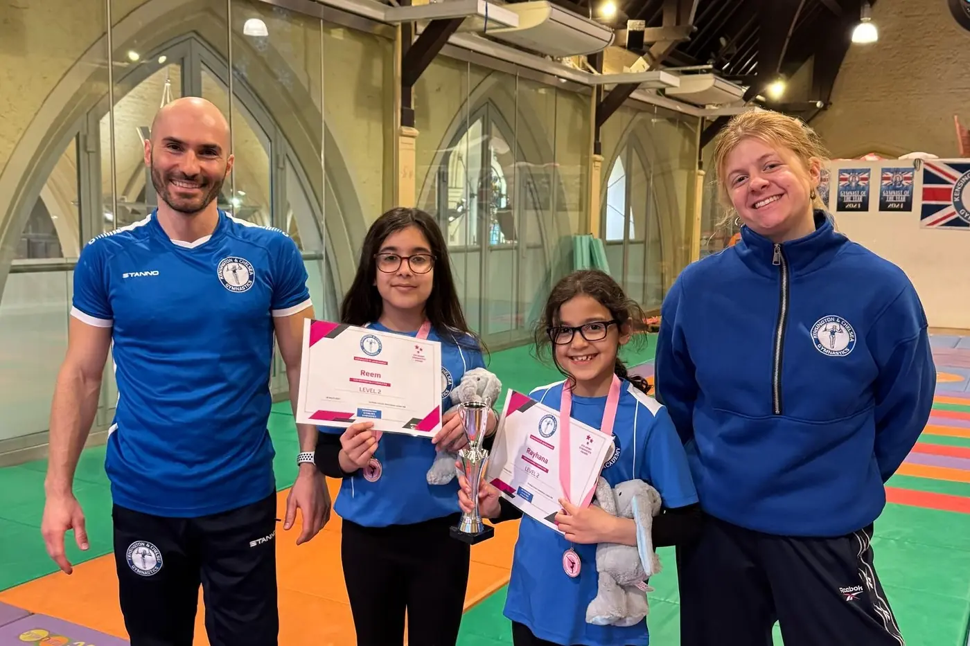 KCGA coaches with two gymnasts holding certificates and awards, featured alongside their family’s testimonial.