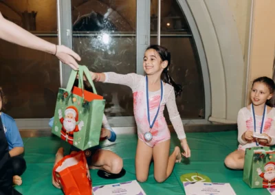 Gymnast receiving a festive gift bag during the Chelsea Gymnastics Academy Christmas event.