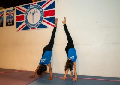 Easter 2025 gymnastics for primary school children – two gymnasts practise wall-supported handstand drills at KCGA in Kensington.