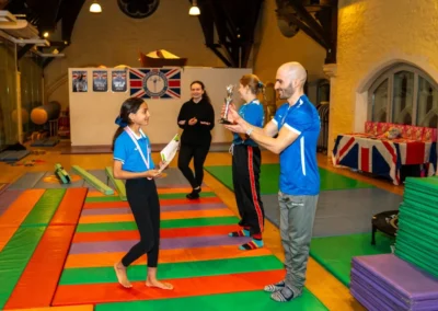 Gymnast receiving Easter 2025 Gymnast of the Term award from KCGA coach at Chelsea House in Kensington London