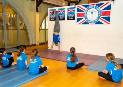 Coach demonstrating a handstand while children watch during Easter 2025 gymnastics classes at KCGA London