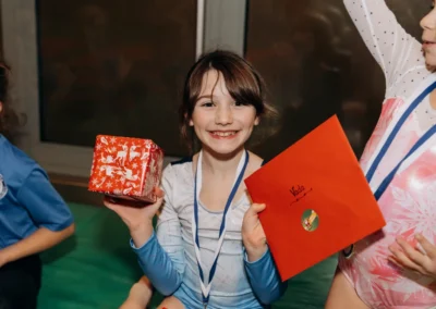 Young gymnast smiling while holding a Christmas present and handwritten card at KCGA’s 2023 event.