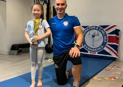 Coach Stefan Kolimechkov with a young student holding a gymnastics trophy during a one-to-one lesson at The Kensington Studio in Kensington W8