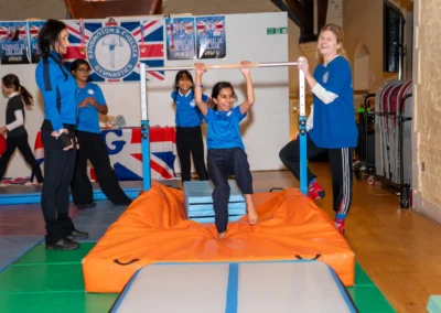 Children practising gymnastics on bars with safety mats and close coach supervision in a recreational class.
