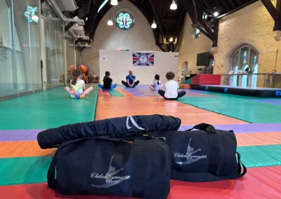 Children attending a KCGA gymnastics class at St Philip’s Church in Kensington W8, sitting on mats during a coached warm-up session.