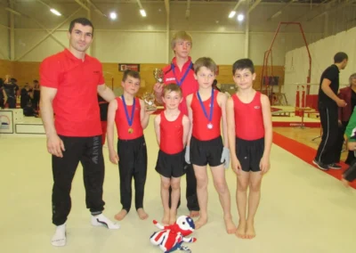Coach Stefan Kolimechkov with boys’ artistic gymnasts holding medals and trophies at the London Regional Gymnastics Championships in 2014