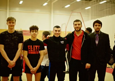 Coach Stefan Kolimechkov with gymnasts and colleagues at the London Gymnastics Championships inside a competition arena.