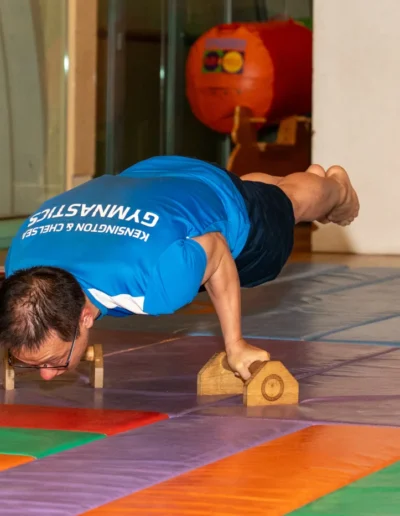 Adult male gymnast performing advanced planche variation on parallettes at KCGA 2025 Annual Performance Kensington London