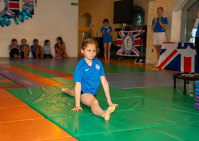 Young gymnast performing front splits on floor mat at KCGA Annual Performance 2025 Kensington