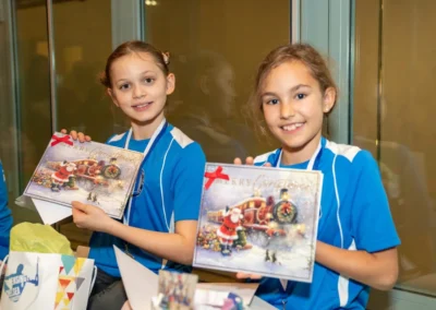 Two girls holding Christmas cards and medals at London gymnastics club Christmas event