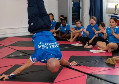 Close-up of Coach Stefan Kolimechkov in a headstand as children watch and clap at More House School, Knightsbridge London