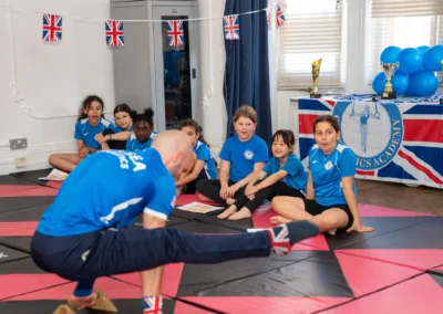 Coach Stefan performing strength gymnastics move in front of children at More House School Knightsbridge SW1X