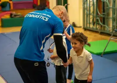 KCGA coach awarding a medal to a young child during Easter Week 2026 at Chelsea gymnastics