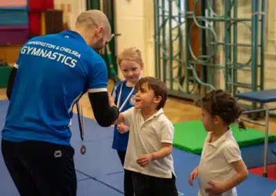 Young children celebrating and giving a high five to a KCGA coach after receiving medals in Chelsea
