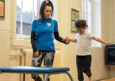 Young child practising the hurdle step from one foot to two feet on a bench before vault during Easter 2026 gymnastics in Chelsea, London SW3