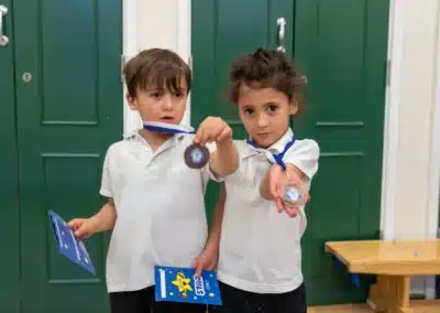 Two young children showing their KCGA Easter Week medals and sticker charts after gymnastics in Chelsea