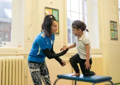 KCGA coach helping a young child prepare for a vault exercise during a Chelsea gymnastics class