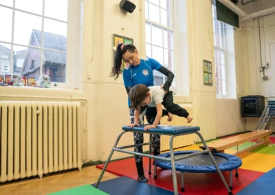 Young boy practising a squat on vault exercise with coach support during a KCGA Chelsea gymnastics class
