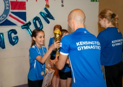 Young gymnast receiving a trophy and certificate from a coach during the KCGA Annual Performance 2025 in Kensington, London.