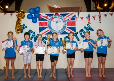 Group of young gymnasts holding certificates, medals and trophies at the KCGA Annual Performance 2025 in Kensington, London.
