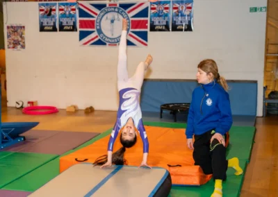 Young gymnast performing a handspring on the air track with coach supervision during KCGA Easter Week 2026 in Kensington