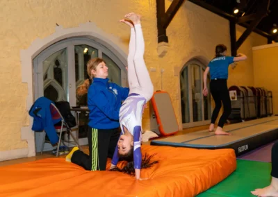 Artistic gymnast practising an assisted back handspring with coach support during gymnastics classes in Kensington London
