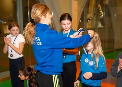 Coach giving medals to primary-school gymnasts during an Easter gymnastics award ceremony in Kensington London