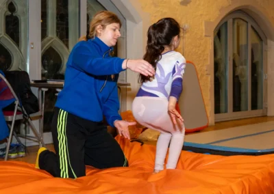Young gymnast leaning backwards into the set position before a back handspring with coach support in Kensington London