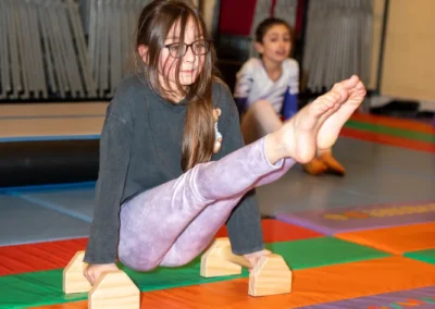 Girl performing an L-sit on wooden parallettes during gymnastics training in Kensington London