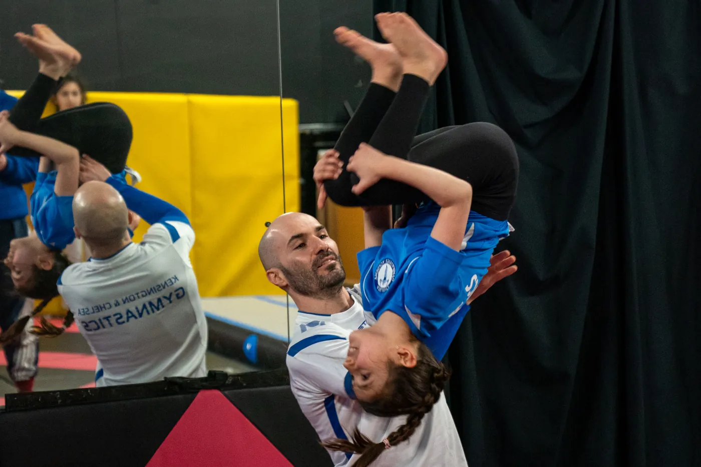 Coach supporting a young gymnast to learn back somersault during Easter Sessions at Kensington & Chelsea Gymnastics Academy in London