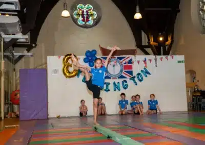 Young gymnast demonstrating flexibility and balance on a beam during the KCGA Annual Performance 2025 in Kensington, London.