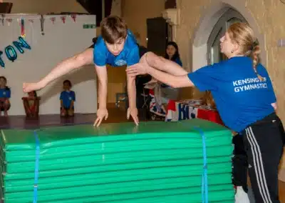 Gymnastics coach supporting a young boy performing a vault skill during KCGA Annual Performance 2025 in Kensington, London.