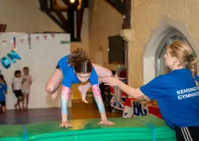 Gymnastics coach supporting a young gymnast during a vault skill at KCGA Annual Performance 2025 in Kensington.