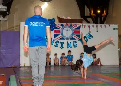 KCGA coach supervising a young gymnast performing a floor skill during the Annual Performance 2025 in Kensington, London.