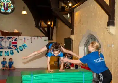 Gymnastics coach supporting a young gymnast during the KCGA Annual Performance 2025 in Kensington, London.
