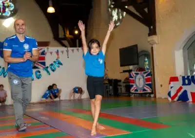 Young gymnast presenting during KCGA Annual Performance 2025 while coach applauds in Kensington, London.