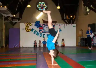 Young gymnast performing a one-handed cartwheel during KCGA Annual Performance 2025 in Kensington, London.