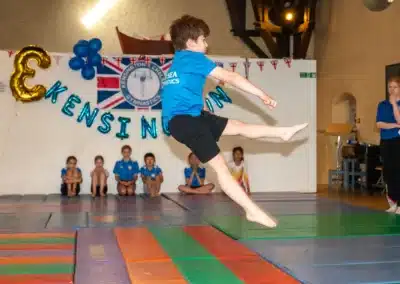 Young gymnast performing a scissor kick jump during KCGA Annual Performance 2025 in Kensington, London.