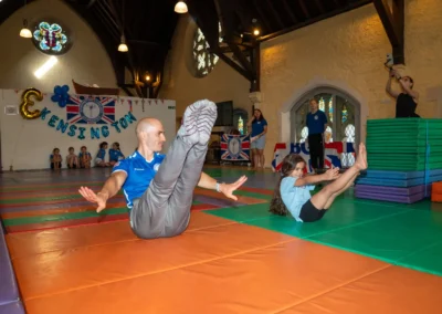 Coach and young gymnast performing V-sit core strength exercise during KCGA Annual Performance 2025 in Kensington, London.