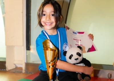 Young gymnast smiling with trophy, medal and certificate after KCGA Annual Performance 2025 in Kensington, London.